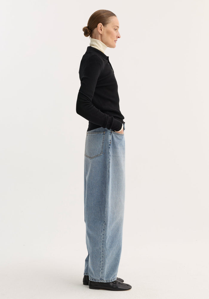 Model in sculptural denim trousers with balloon leg, high waist, and relaxed fit, paired with a layered black ribbed top, showcasing a modern silhouette.