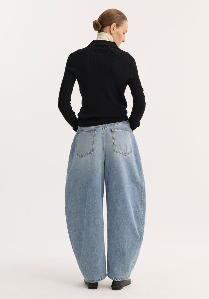 Model wearing Sculptural denim trousers | classic blue, showcasing their balloon leg and high waist, paired with a black fitted top and ankle boots.