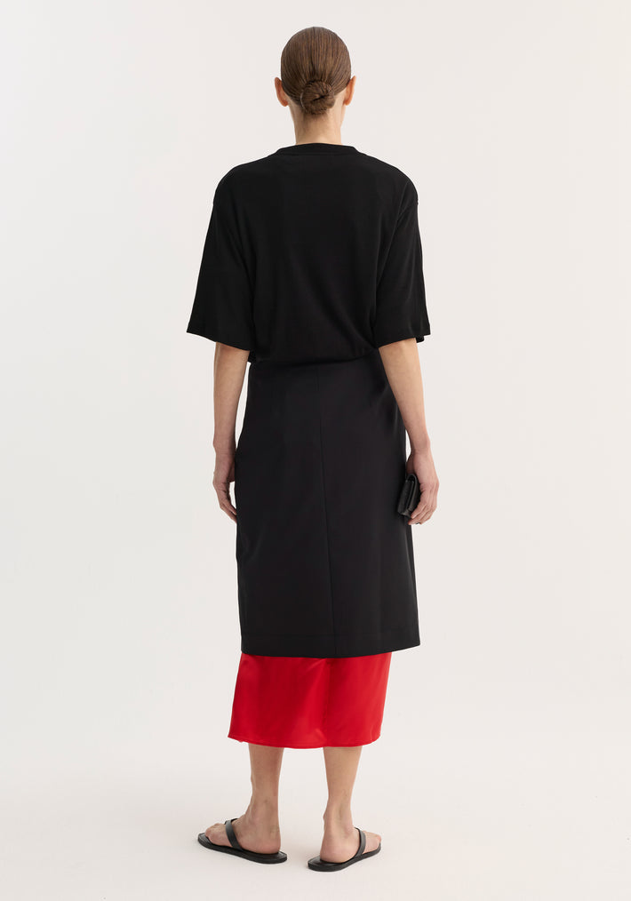 Contrast upside-down skirt | black, shown from the back, featuring a tapered silhouette with a front slit and a bold red underlayer, worn with black sandals.