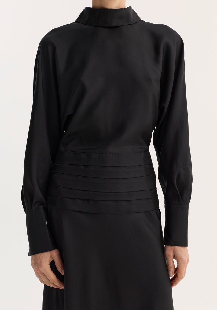 Model wearing the Tuxedo silk dress in black, featuring a high reversed collar, pleated cummerbund waist, and smooth, flowing long sleeves.