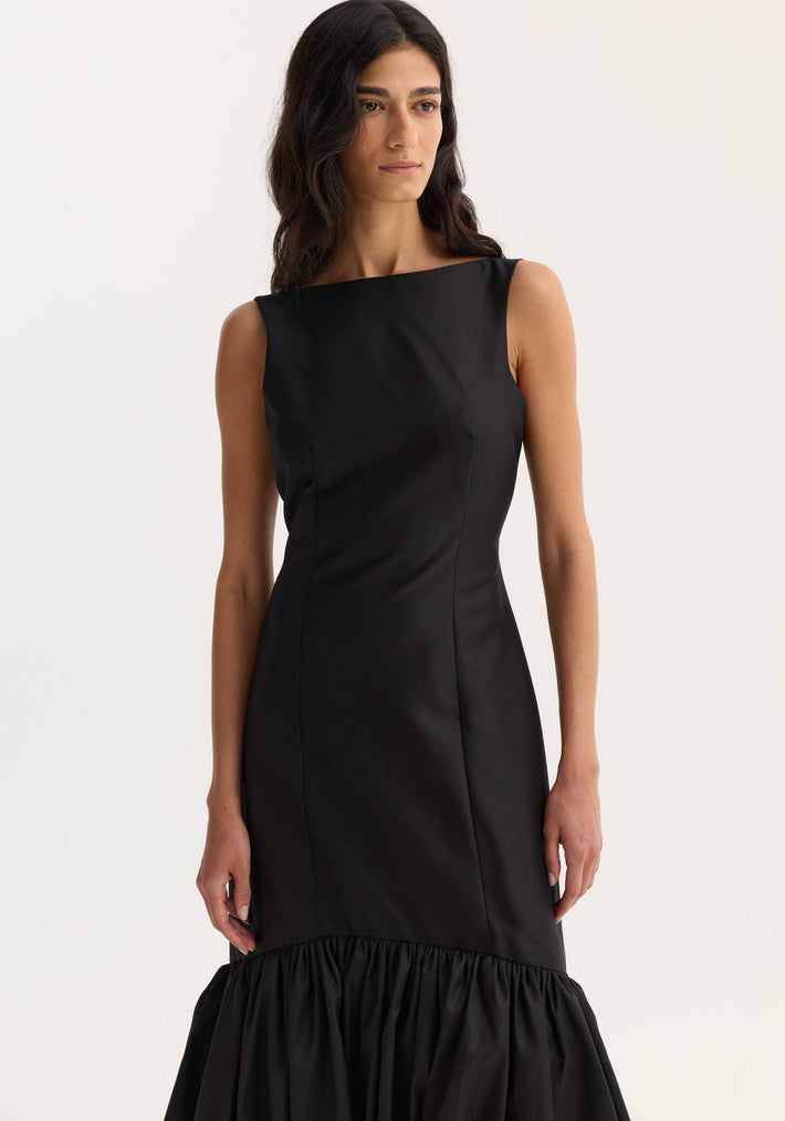 Voluminous dress | black, featuring a sleeveless, form-fitting design with a boat neckline and peplum hem. Tailored seams accentuate the model's silhouette.