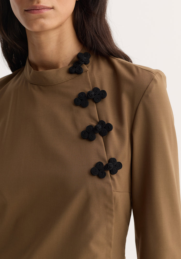 Pankou closure dress | mocha: Close-up of a camel-brown blouse or jacket with distinctive black pankou closures spiraling down from a high neckline.