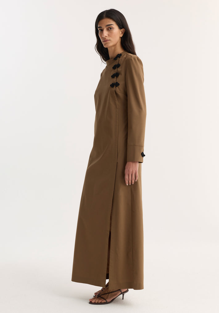 Model in Pankou closure dress | mocha, featuring asymmetrical pankou button details, floor-length with side split, long sleeves, paired with black heeled sandals.