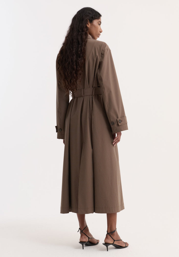 Woman in a Technical check belted coat, brown multi check, with ankle-length, self-belt, pleats, buttoned cuffs, and kitten-heel sandals, viewed from behind.