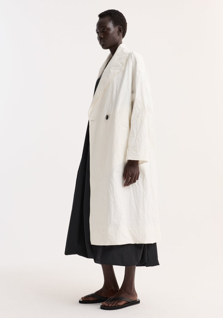 Model in profile wears an oversized crushed cotton coat with raglan sleeves and a single black button, over a black skirt.