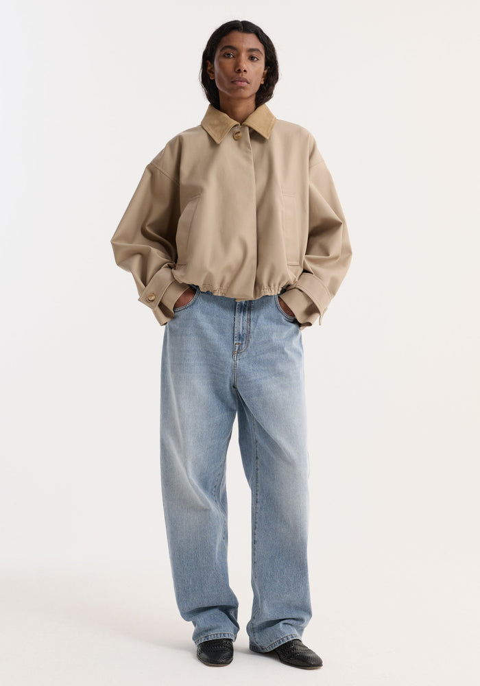 Model wearing a Suede Collar Blouson Jacket in sand, featuring a cropped design, suede collar, wide sleeves, and hidden closure, paired with loose blue jeans and black loafers.