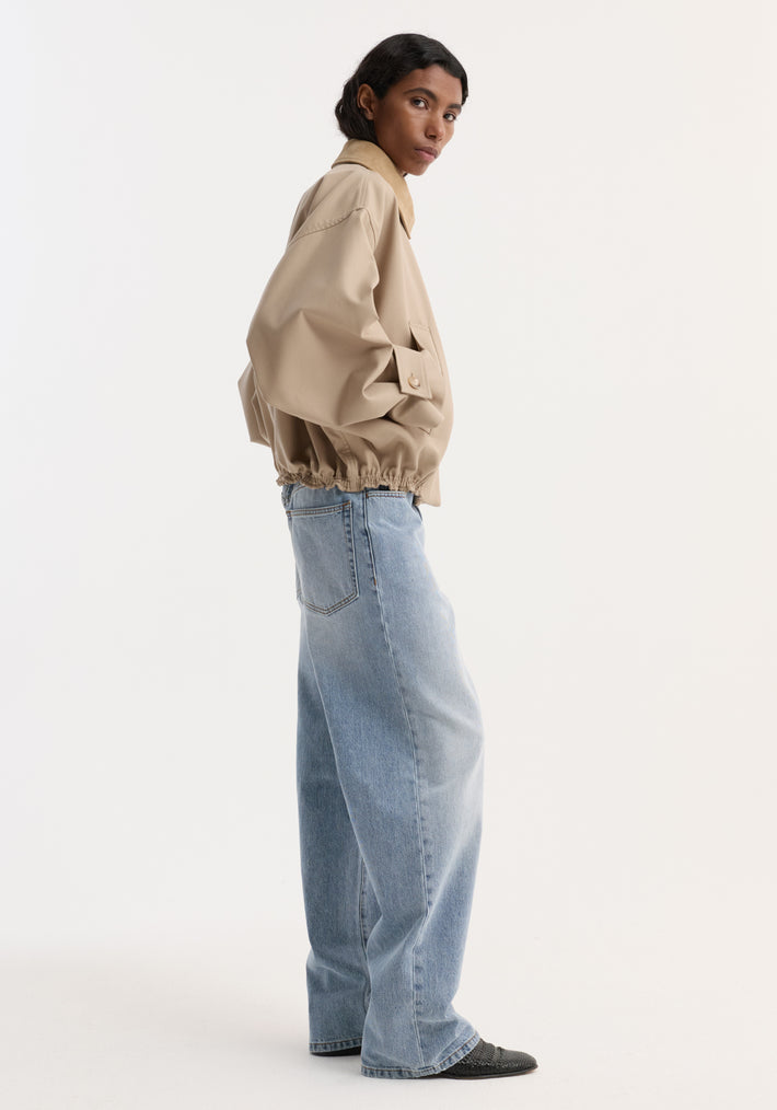 Person in profile wearing a Suede collar blouson jacket | sand, showcasing cropped trench-inspired design with wide sleeves and suede collar, hands in pockets.