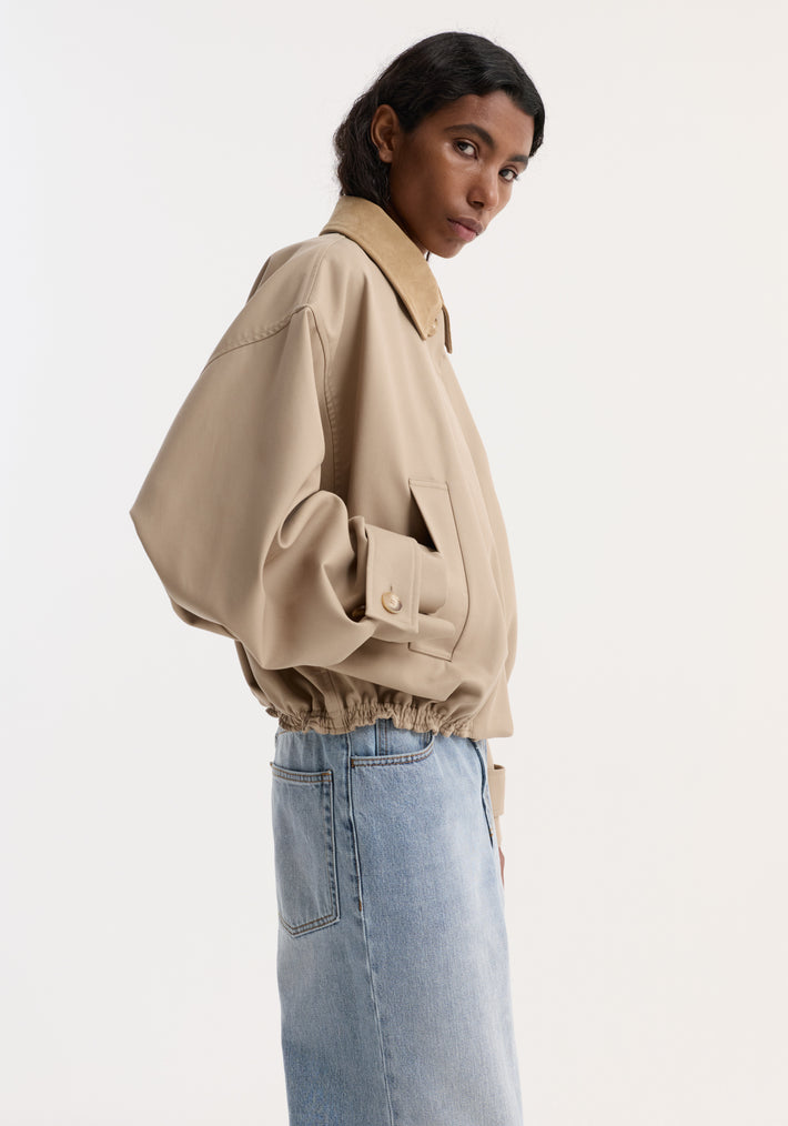 Side-profile of a model wearing a Suede collar blouson jacket | sand, showcasing its cropped, wide sleeves, and suede collar against a plain backdrop.