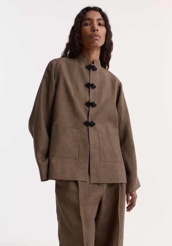 Model wearing Pankou closure linen jacket in brown melange, featuring a mandarin collar, frog-style closures, patch pockets, and wide-leg trousers. Crafted from 100% European flax linen.