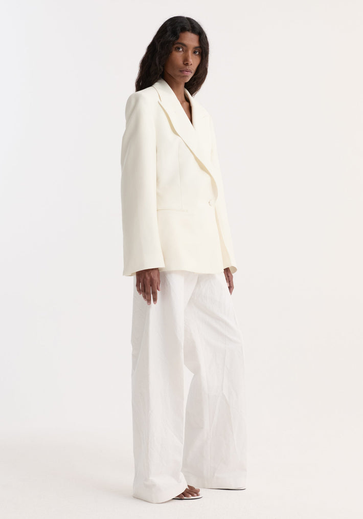 Model wearing Hourglass shaped blazer in off white, featuring a cinched waist, sharp notch lapel, and single button closure, paired with wide-leg trousers.