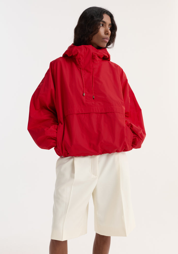 Volume silk-blend anorak in red, featuring a hood, front pocket, zippered side pockets, and adjustable hood drawcords, modeled with off-white knee-length shorts.