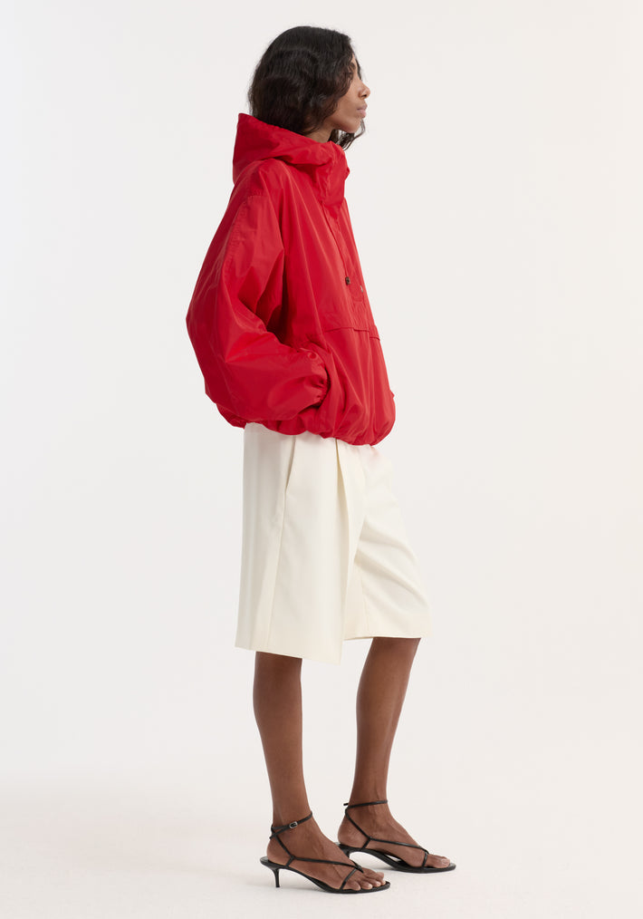 Volume silk-blend anorak in red, featuring a hood, front and side pockets, paired with white shorts and black sandals against a light background.
