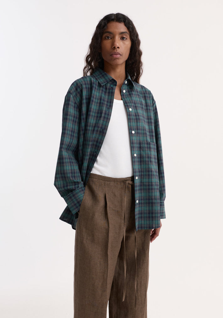 Woman modeling an Oversized check shirt | retro green check, unbuttoned over a white tank top, paired with high-waisted, wide-leg brown trousers.