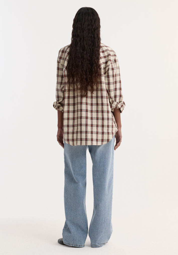 Person wearing an oversized check shirt in red table check pattern, showcasing its relaxed fit with rolled-up sleeves, paired with light-wash jeans.