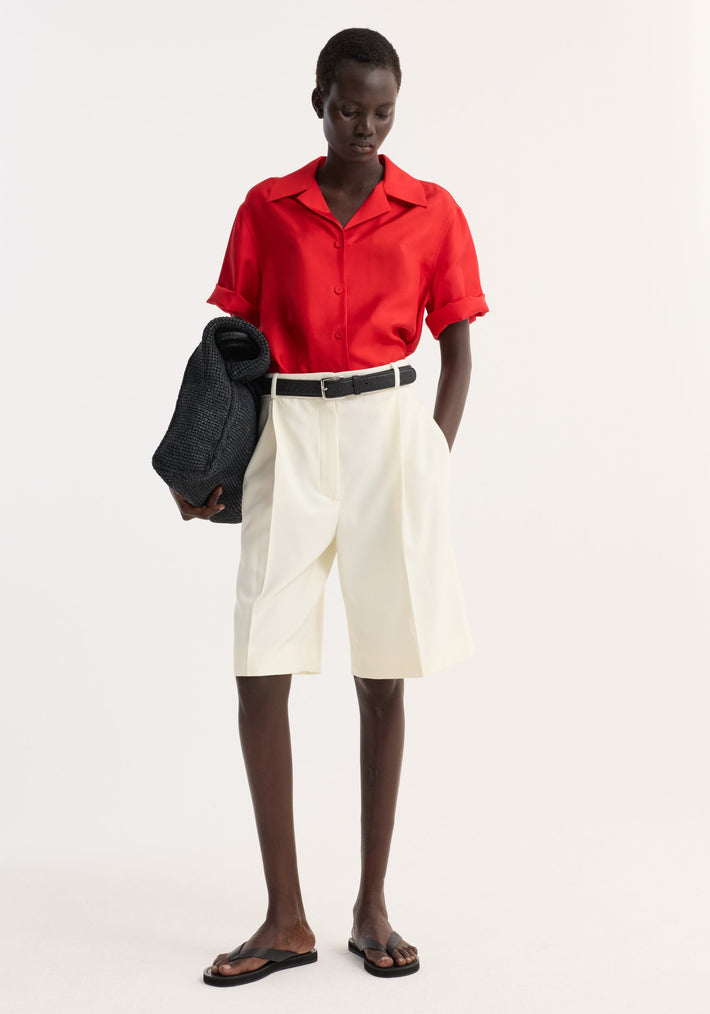 Model wearing Camp collar silk shirt | red, paired with tailored shorts, black belt, sandals, and carrying a slouchy tote. Casual, summery look.