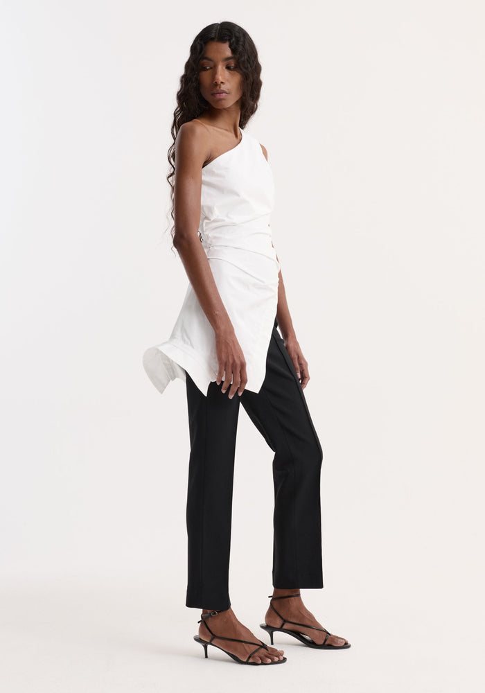 Model wearing Reimagined one shoulder top | optic white, featuring asymmetrical hem and deconstructed detailing, paired with slim-leg trousers and strappy sandals.
