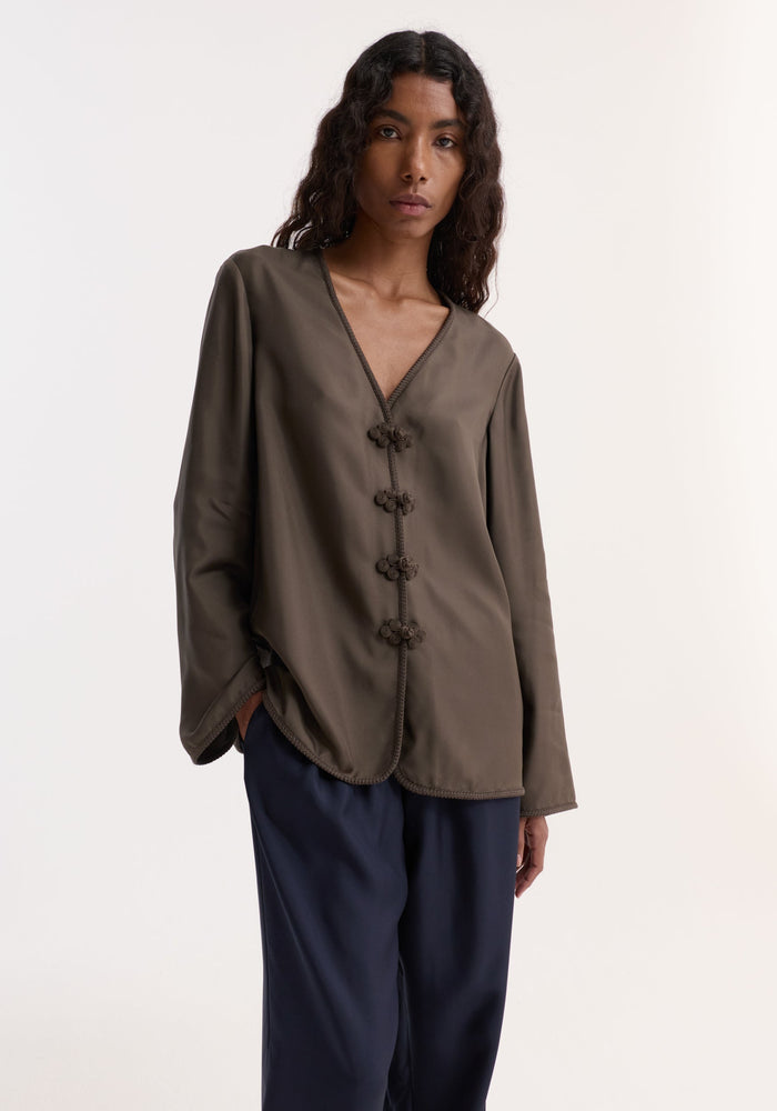 Model in Pankou closure silk top with knotted buttons, relaxed fit, embroidered edges, paired with dark navy wide-leg trousers, showcasing a casual-chic look.
