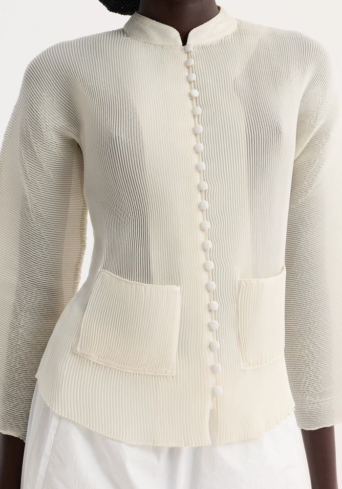 Model wears a Plissé cardigan | cream, featuring a mandarin collar, fabric-covered buttons, micro-pleated texture, and patch pockets, paired with a white bottom.