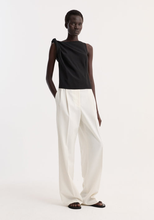 Fashion model wearing Draped linen silk top | black, featuring a twist detail on one shoulder, paired with high-waisted wide-leg trousers.