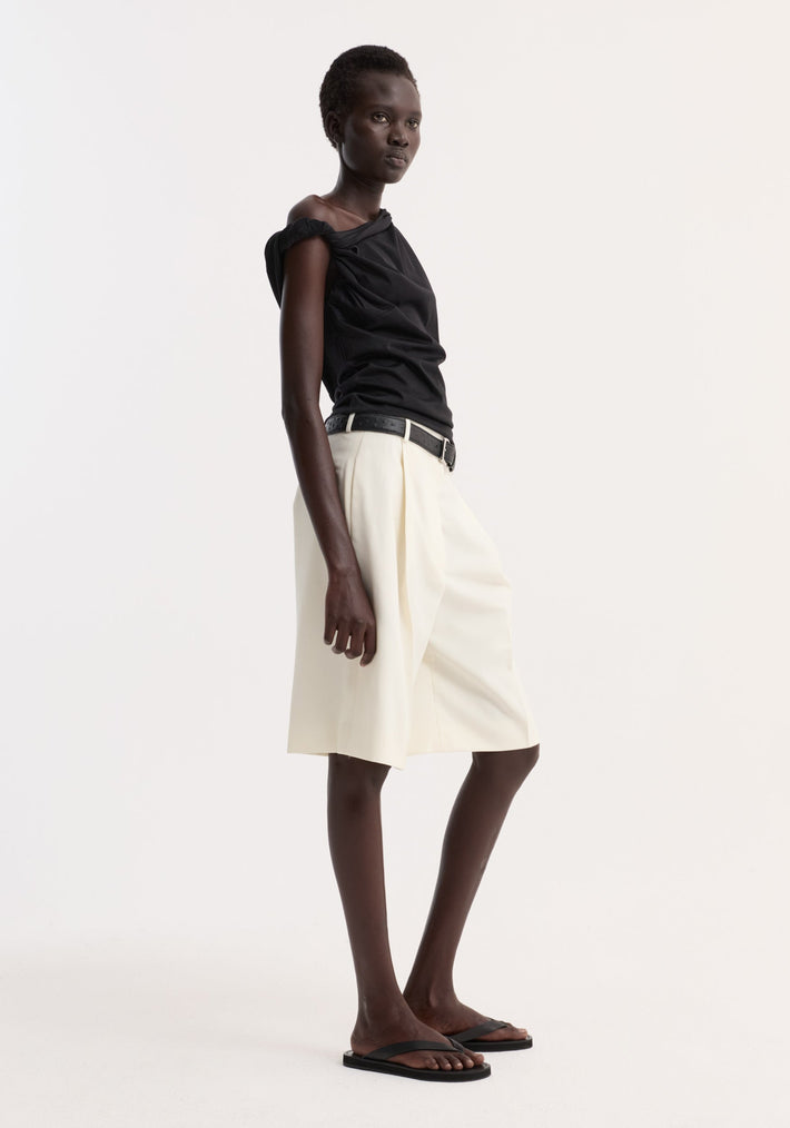 Model in Sculptural cotton silk top showcasing its sleeveless design and off-shoulder twist detail, paired with high-waisted shorts and black sandals.