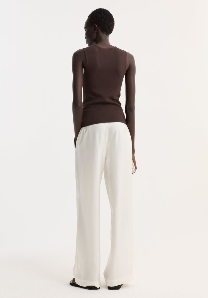 Person wears Bustier shaped knitted top in dark chocolate, showcasing its fitted design and bustier neckline, paired with high-waisted trousers and sandals.