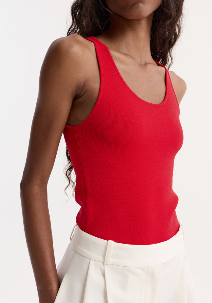 Person wearing a fitted Scoop Neck Knitted Top in red, showcasing its rib-knit texture and bustier neckline, paired with high-waisted, off-white trousers or skirt.
