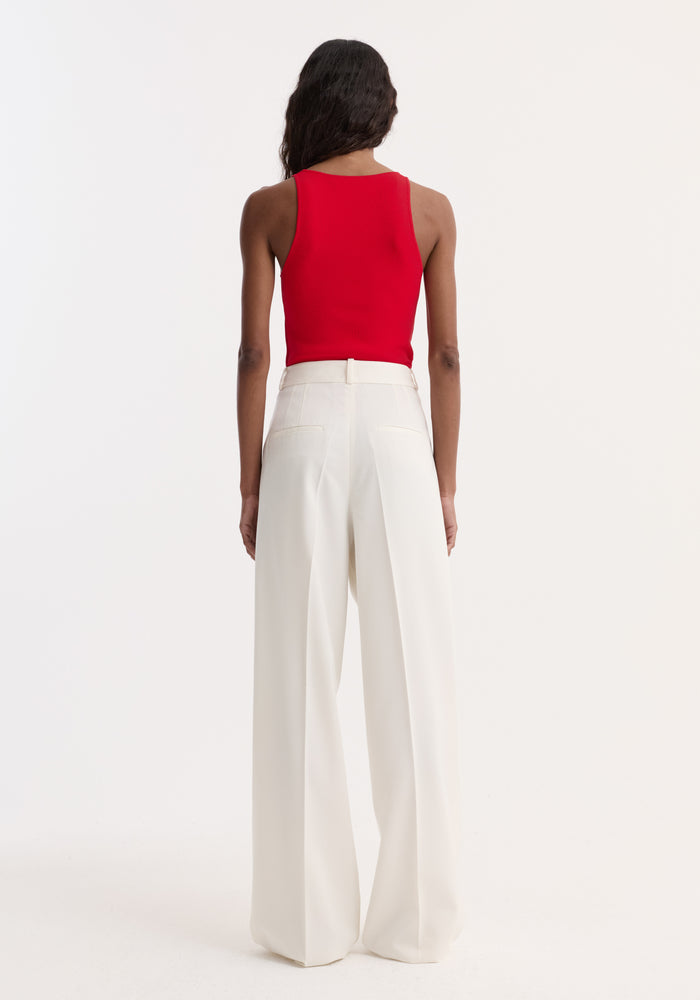 Person wearing the Scoop neck knitted top | red, featuring a sleeveless, fitted design with a bustier neckline, paired with high-waisted, wide-leg white trousers.