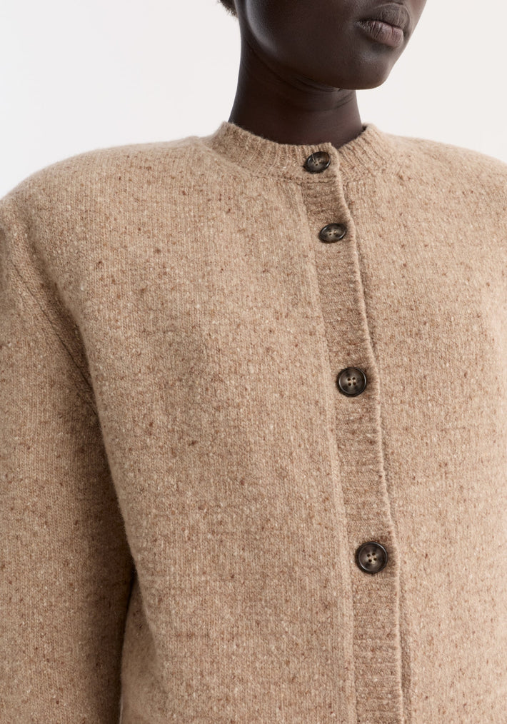 Fine merino tweed cardigan in oat melange with dark buttons, round neckline, and shoulder pads; slightly cropped, showcasing soft, fuzzy texture.