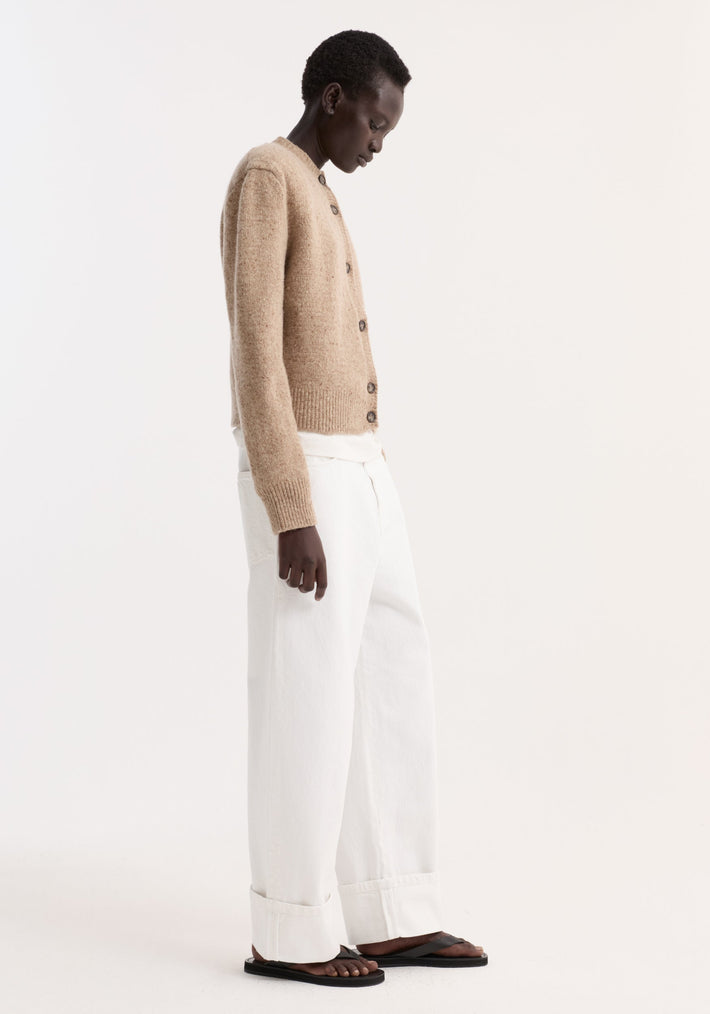 Fine merino tweed cardigan in oat melange with shoulder pads, worn by a model in profile, paired with white T-shirt and wide-leg trousers.