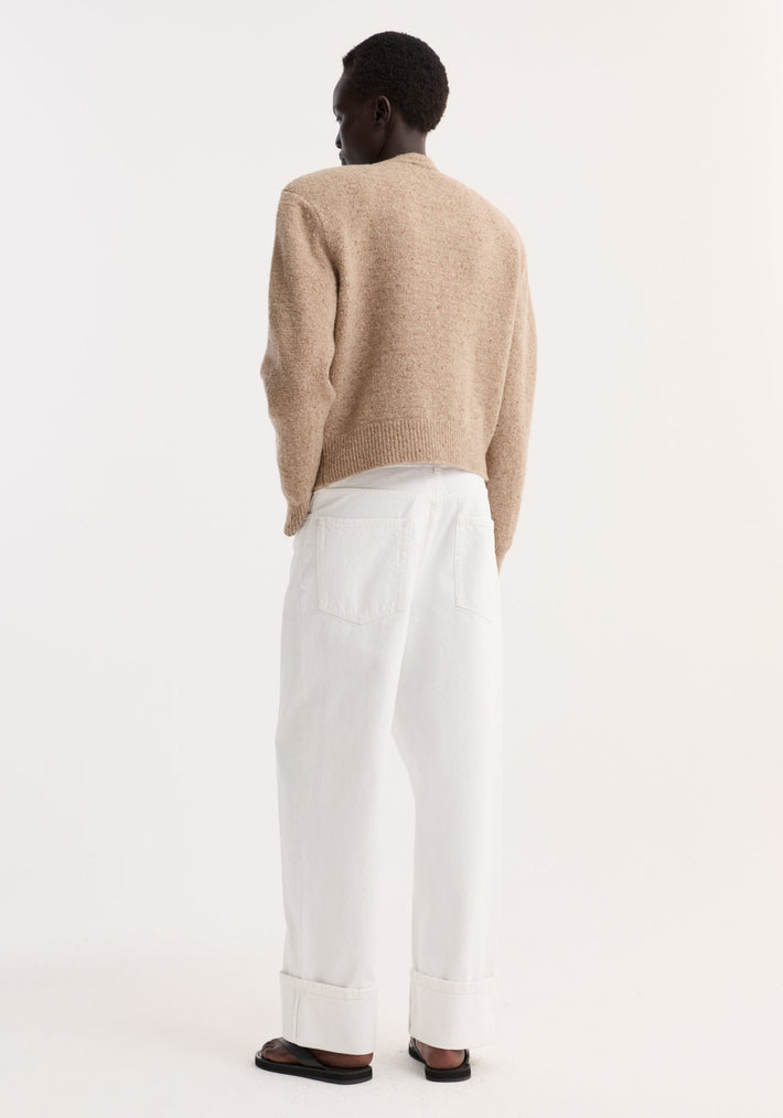Person in Fine merino tweed cardigan | oat melange, cropped with shoulder pads, paired with high-waisted trousers and black sandals, showcasing minimalist style.