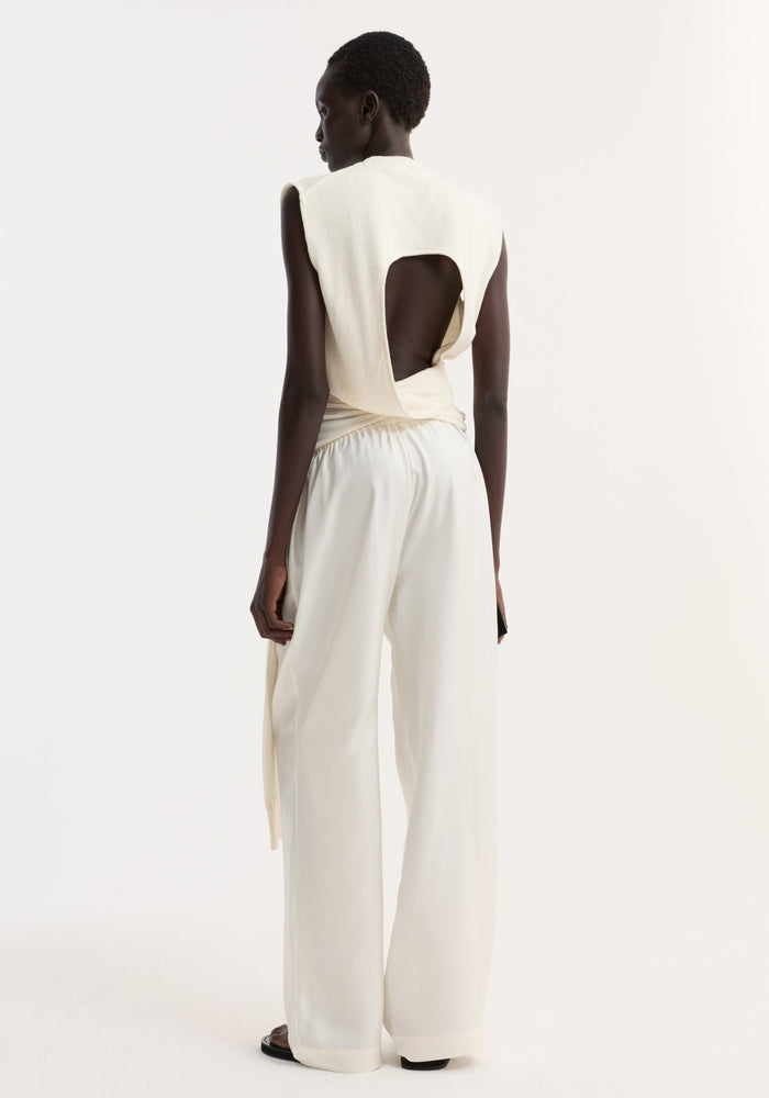 Model wearing Open back knitted wrap top with deconstructed sleeves, tied at waist, paired with wide-leg trousers and black sandals, showcasing minimalist style.