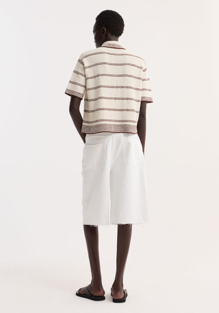 Model wearing Towelling striped polo in cream/brown with a cropped fit, polo collar, four-button placket, paired with white Bermuda shorts and black slide sandals.