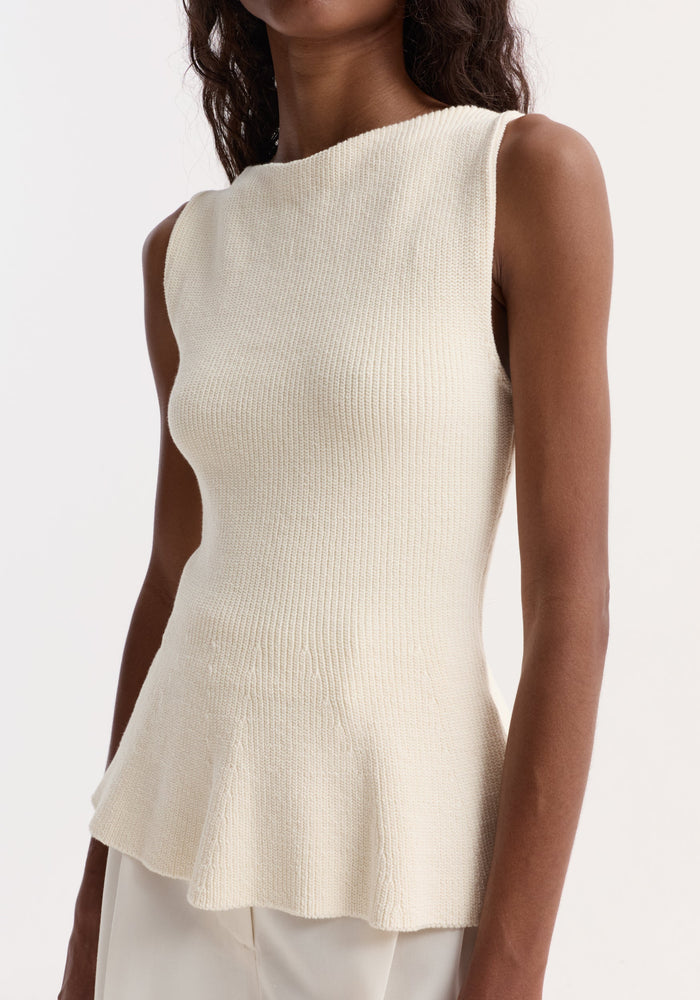 Sculptural knitted top | cream: Sleeveless off-white cotton top with boat neckline and peplum flare, modeled on a slender figure partially showing white trousers or skirt.