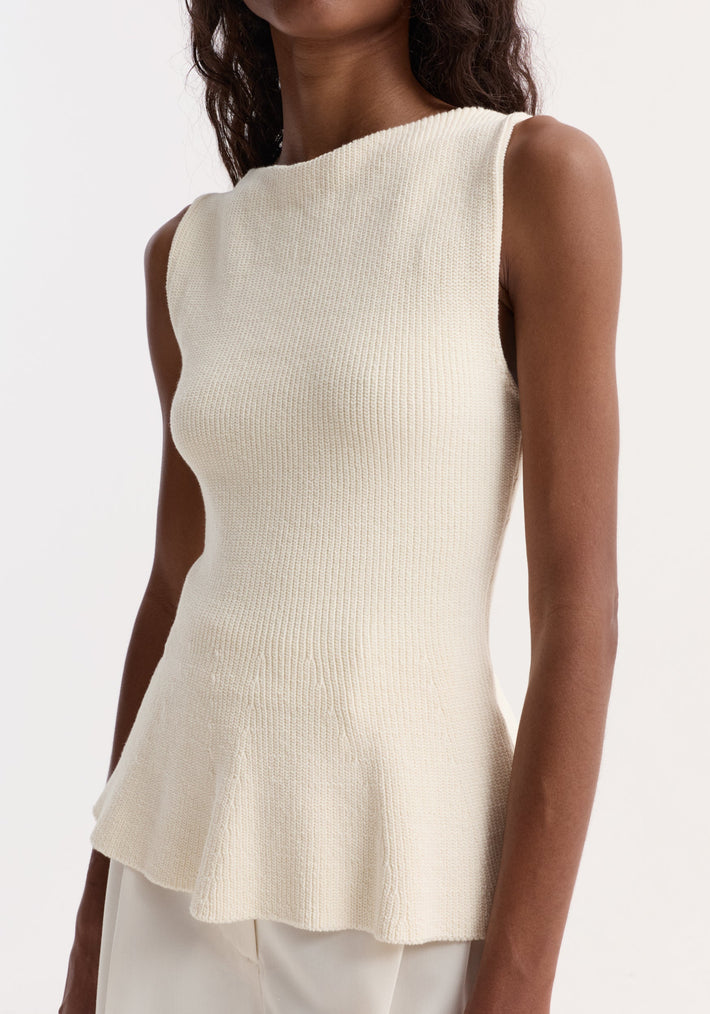 Sculptural knitted top | cream: Sleeveless off-white cotton top with boat neckline and peplum flare, modeled on a slender figure partially showing white trousers or skirt.