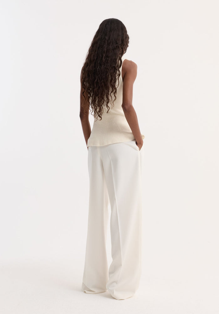 A woman models the Sculptural knitted top | cream, showcasing its boat neckline and peplum design, paired with high-waisted, wide-leg trousers.