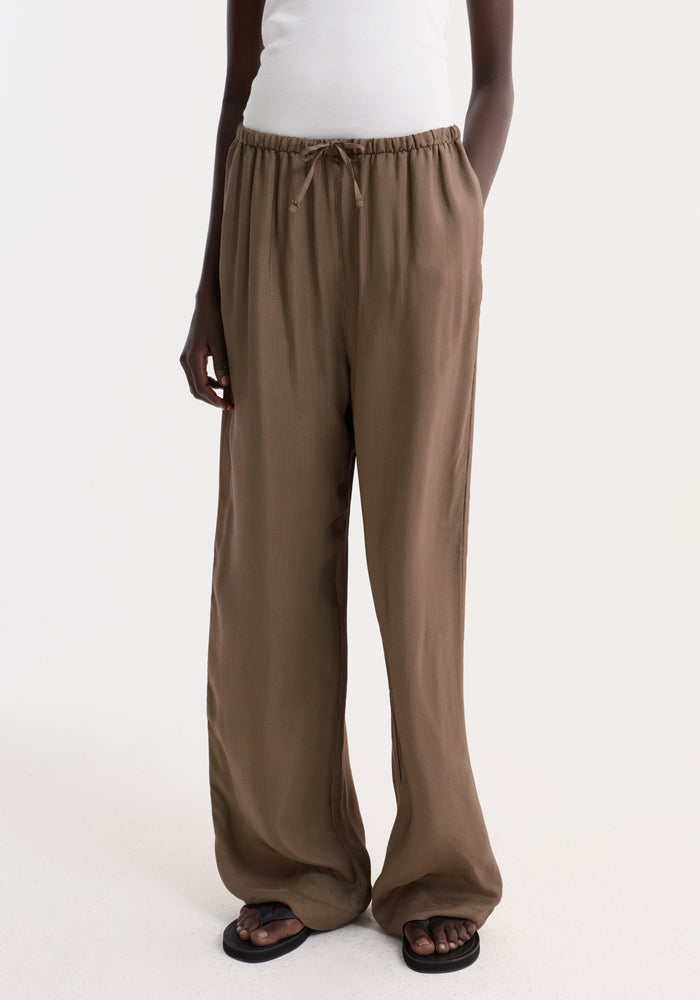 Person wearing Relaxed fit trousers | brown mini check with wide legs and a drawstring waistband, styled with side pockets and black flip-flop sandals.