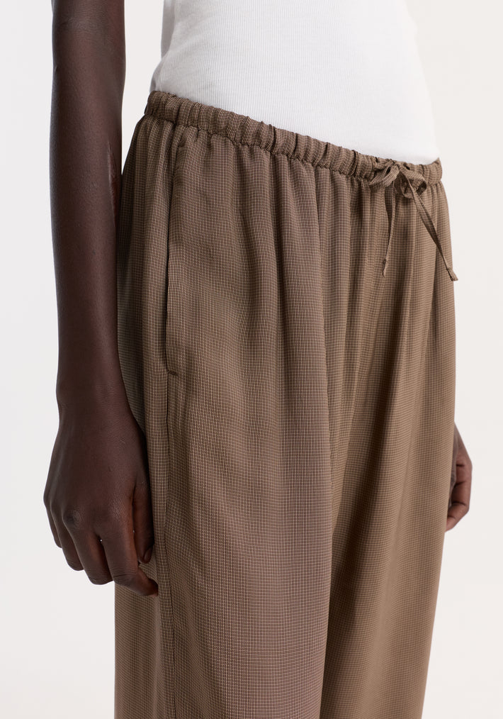 Person wearing relaxed fit trousers with a mini check pattern, featuring a drawstring waistband and wide legs, showcasing a reimagined classic pyjama style.