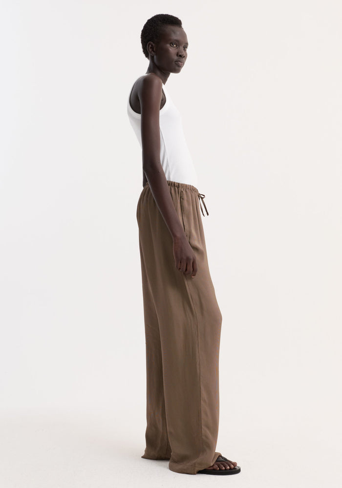Model wearing Relaxed fit trousers in brown mini check with a wide leg and drawstring waistband, paired with a white ribbed tank top and black flip-flops.