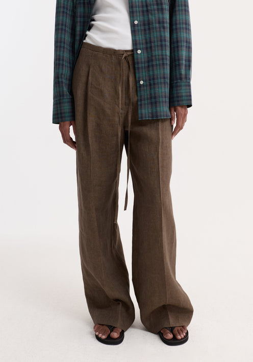 Woman wearing Relaxed drawstring trousers in brown melange with a wide leg and drawstring waistband, styled with a plaid shirt and sandals.