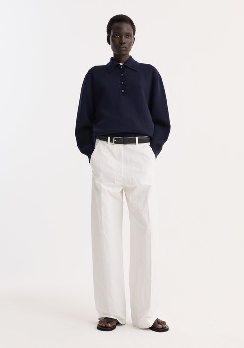 Model wearing Classic baggy chino in optic white, featuring high-waisted wide-leg design, paired with a navy knit polo sweater and black leather belt.