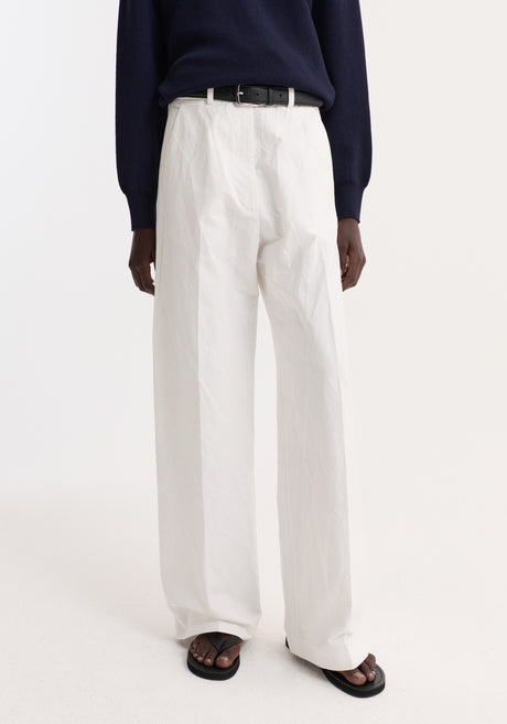 Model wearing Classic baggy chino in optic white, featuring high-waisted wide-leg design, paired with a navy knit polo sweater and black leather belt.