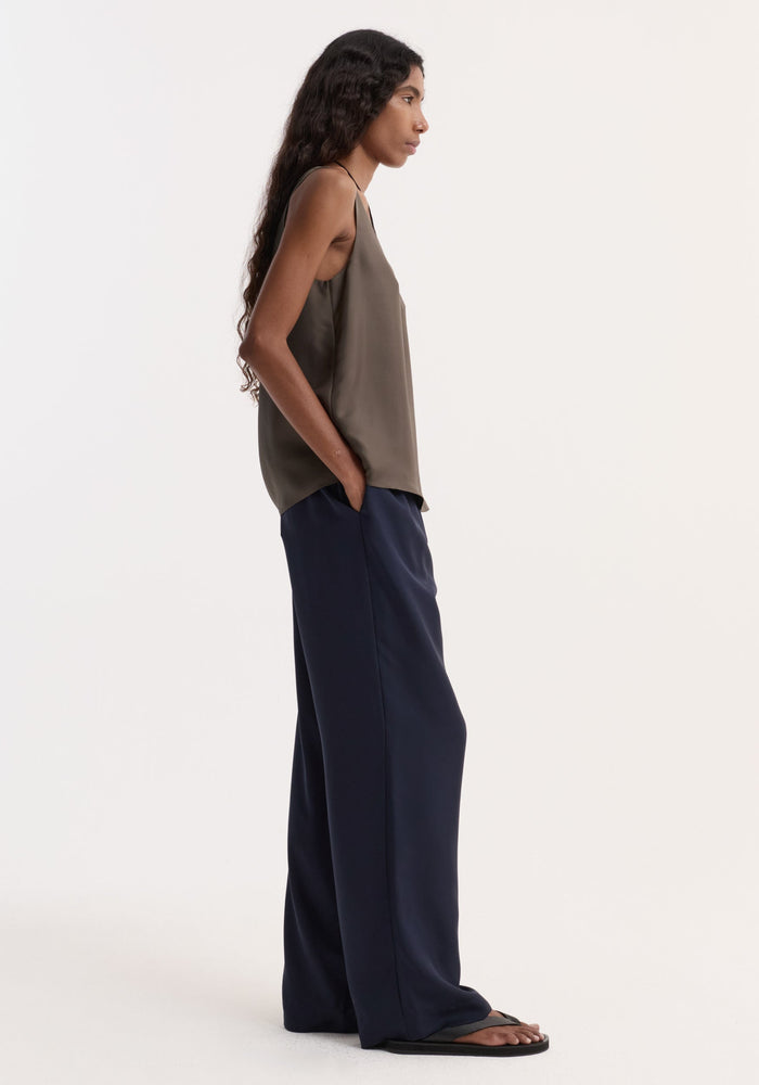 Silk pyjama trousers | night shown on a model with wide-leg design, elastic waistband, faux fly, and two-button detail, styled with an olive tank top.