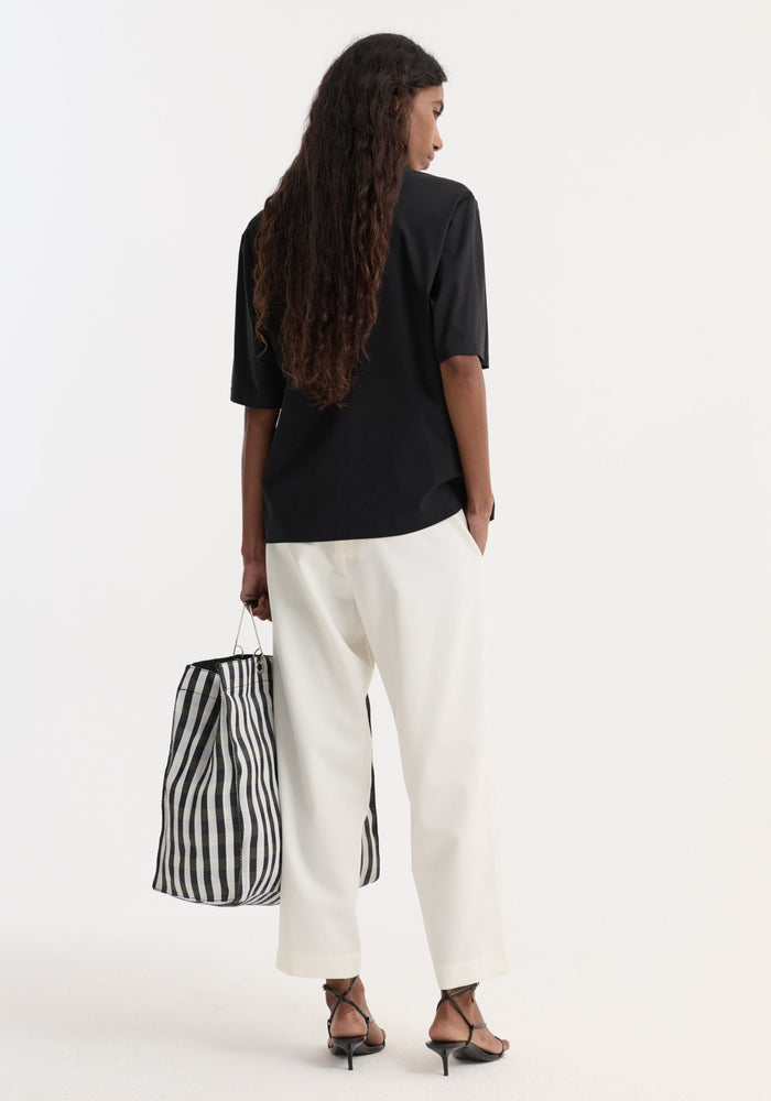 Woman wearing cropped wide leg trousers with an elasticated waist and side pockets, paired with black sandals and holding a striped tote bag.