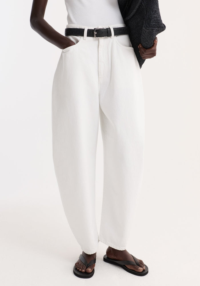 High-waist sculptural denim in optic white, featuring a bold balloon leg and relaxed fit, styled with a black belt and sandals.