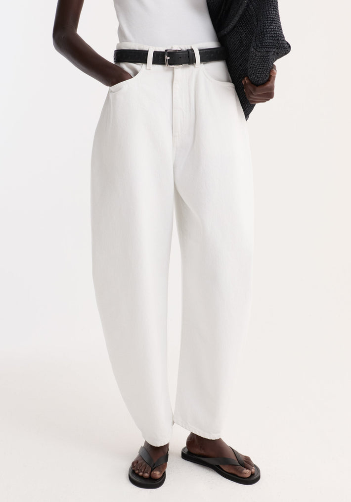 High-waist sculptural denim in optic white, featuring a bold balloon leg and relaxed fit, styled with a black belt and sandals.