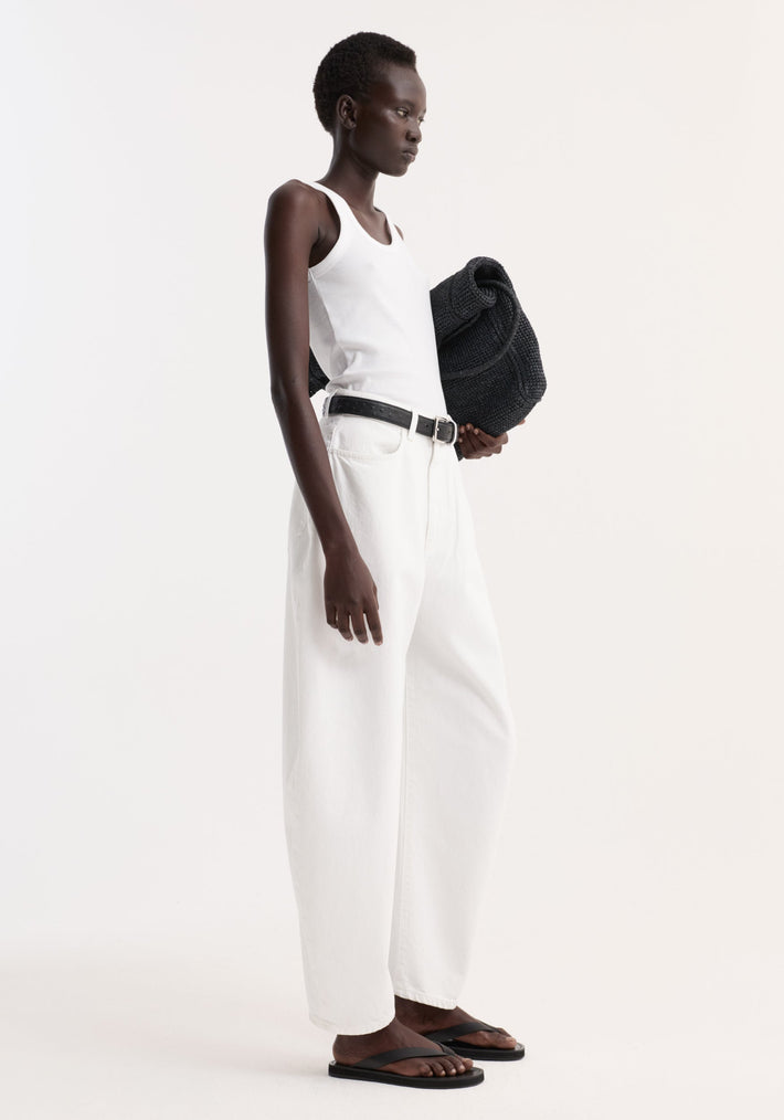 High-waist sculptural denim in optic white, featuring a balloon leg and relaxed fit, worn with a black belt, black sandals, and a draped sweater.