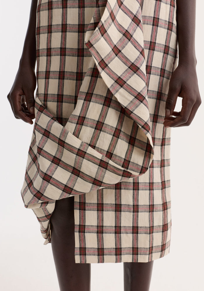 Draped check skirt | red table check features a knee-length, wrap-style design with draped front detail, revealing a thigh slit on a dark-skinned model.