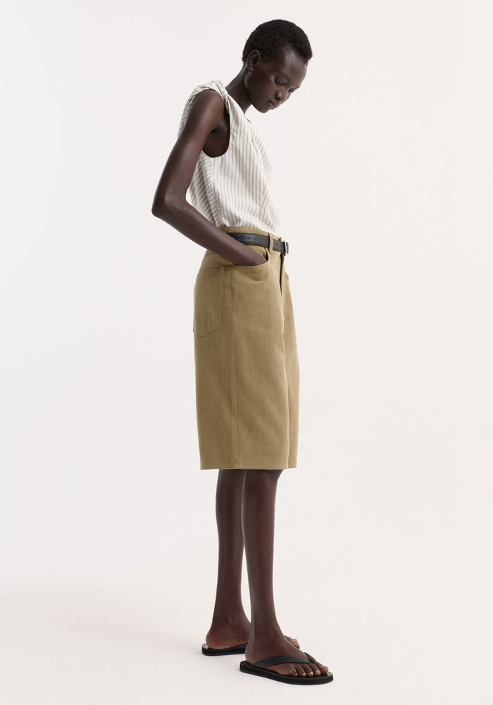 Model in ivory pinstripe top and olive skirt, highlighting Baggy fit denim shorts | sage, showcasing a relaxed, timeless look with patch pockets and a black belt.