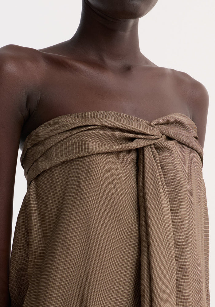 Person wearing Sarong top | brown mini check, featuring a strapless design with a sarong-style twist knot and front slit, highlighting its draped, sculptural effect.