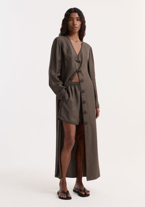 Model wears Taped silk shorts | earth with an elasticated waistband, pleated silk design, and embroidered hem, paired with a matching duster-style coat.